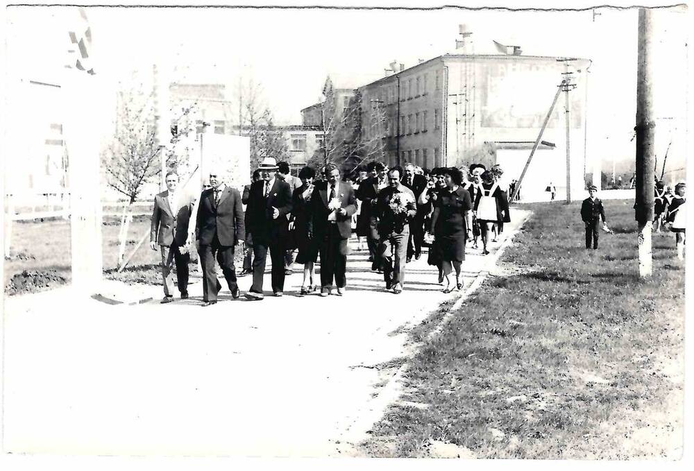 Фото черно-белое. Изображена группа людей, движущихся по тротуару 