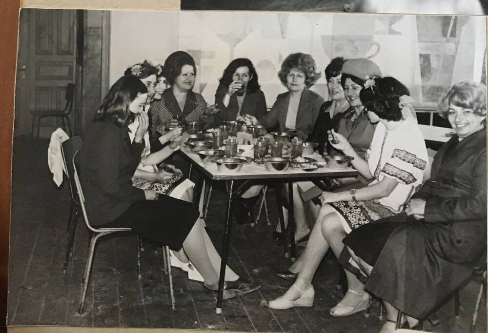 Фото черно-белое, горизонтальное. На снимке, вокруг стола, сидят девушки и женщины.