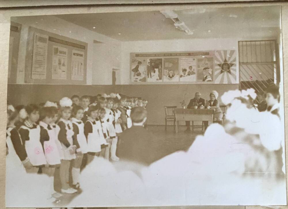 Фото черно-белое, горизонтальное. На снимке  в помещении  коридора школы  слева  и справа стоят школьники.