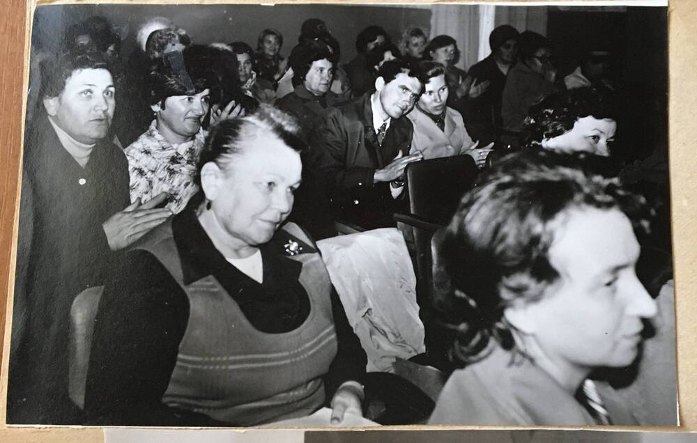 Фото черно-белое, горизонтальное. На фото в зале  на откидных стульях, стоящих рядами, сидят люди.
