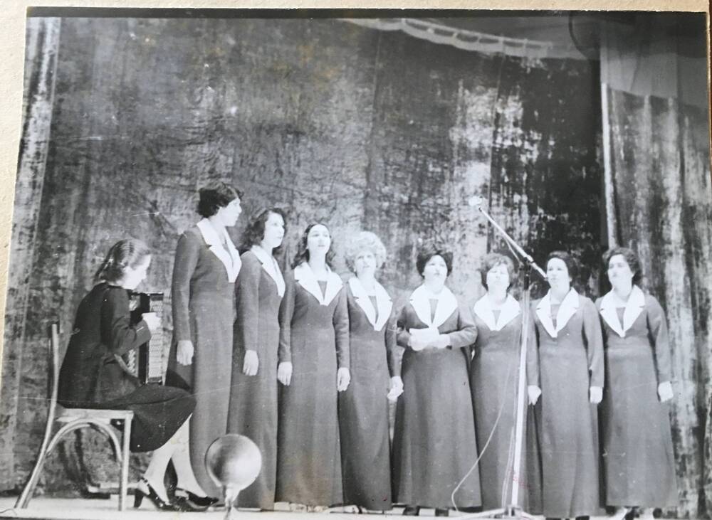 Фото черно-белое, горизонтальное. На сцене стоят в ряд из восьми женщин.
