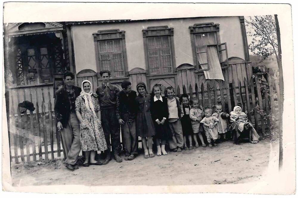 Фотография черно-белая. Вдоль деревянного забора изображена семья.