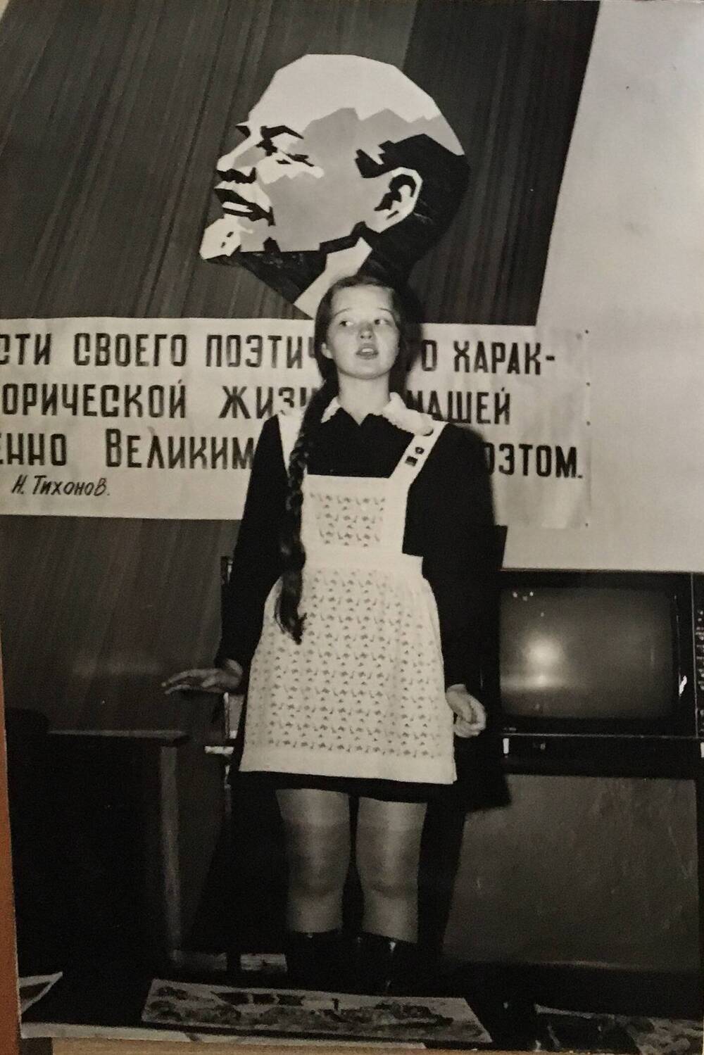 Фото черно-белое, вертикальное. На фото девушка в школьном черном платье и белом фартуке.