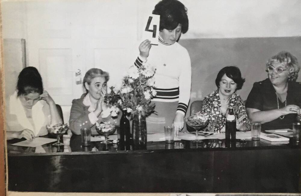 Фото черно-белое, горизонтальное. Изображен стол, за которым сидят четыре женщины.