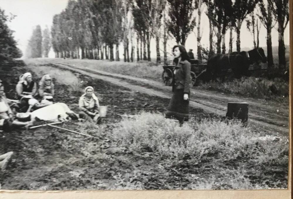 Фото черно-белое, горизонтальное. На фото на обочине дороги сидят женщины.