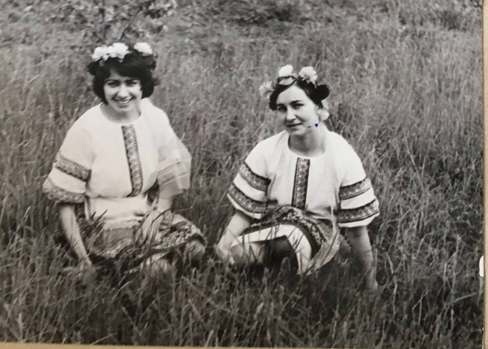Фото черно-белое, горизонтальное. На фото, на фоне поля, сидят две девушки.