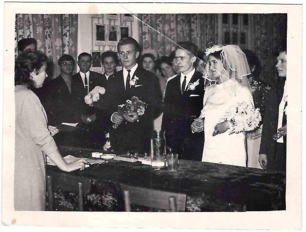 Фотография черно-белая. Изображены жених и невеста, стоящие пред столом. 