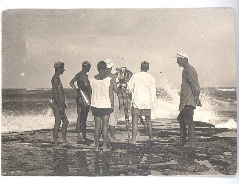 Фотография ч/б. Съемка фильма «Черная пасть» (реж. А.Разумный). Съемочная группа соит с камерой на берегу моря.