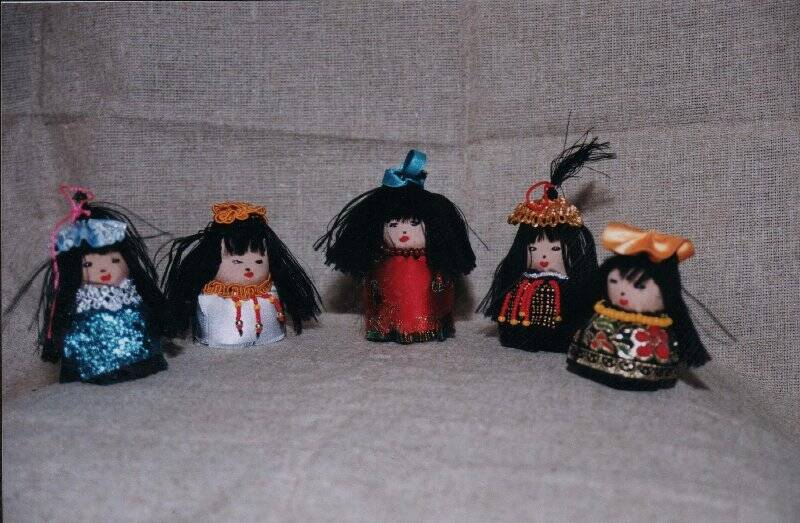 Фотография: Куклы -девочки 2004 г. фотография цветная. На сером фоне сфотографированы куклы - девочки 5 штук. У всех черные, распущенные волосы с бантиками на макушках. Куклы сувенирные. Автор Тогочоева Д.Я.