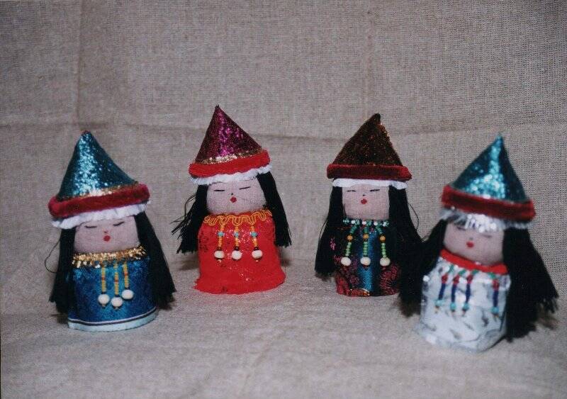 Фотография: Четыре куклы в шапках 2004 г. Фотография цветная. На сером фоне сфотографированы четыре куклы - алтайки. Все в шапках конусовидной формы, с длинными распущенными волосами. Автор Тогочоева Д.Я.