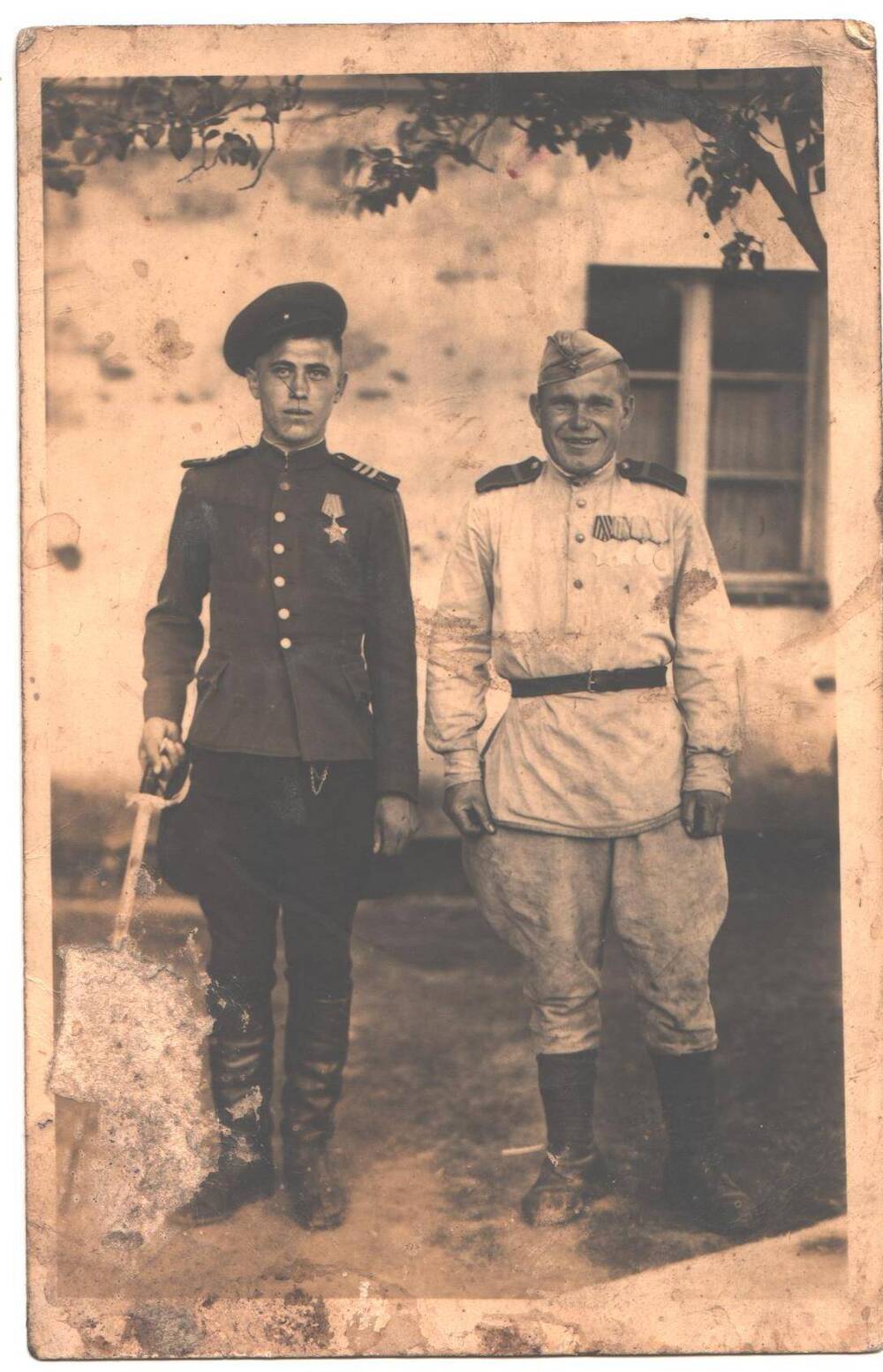 Два молодых человека в военной форме участники Отечественной войны, стоят у каменного дома.