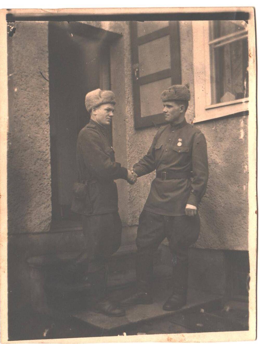 Двое молодых мужчин в военной форме стоят на крыльце у дома, здороваясь за руку. Годы службы в армии город Зоненберг.