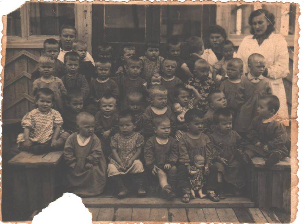 Группа детей ясельного возраста с воспитателями. Снимок сделан на крыльце здания детского сада. 