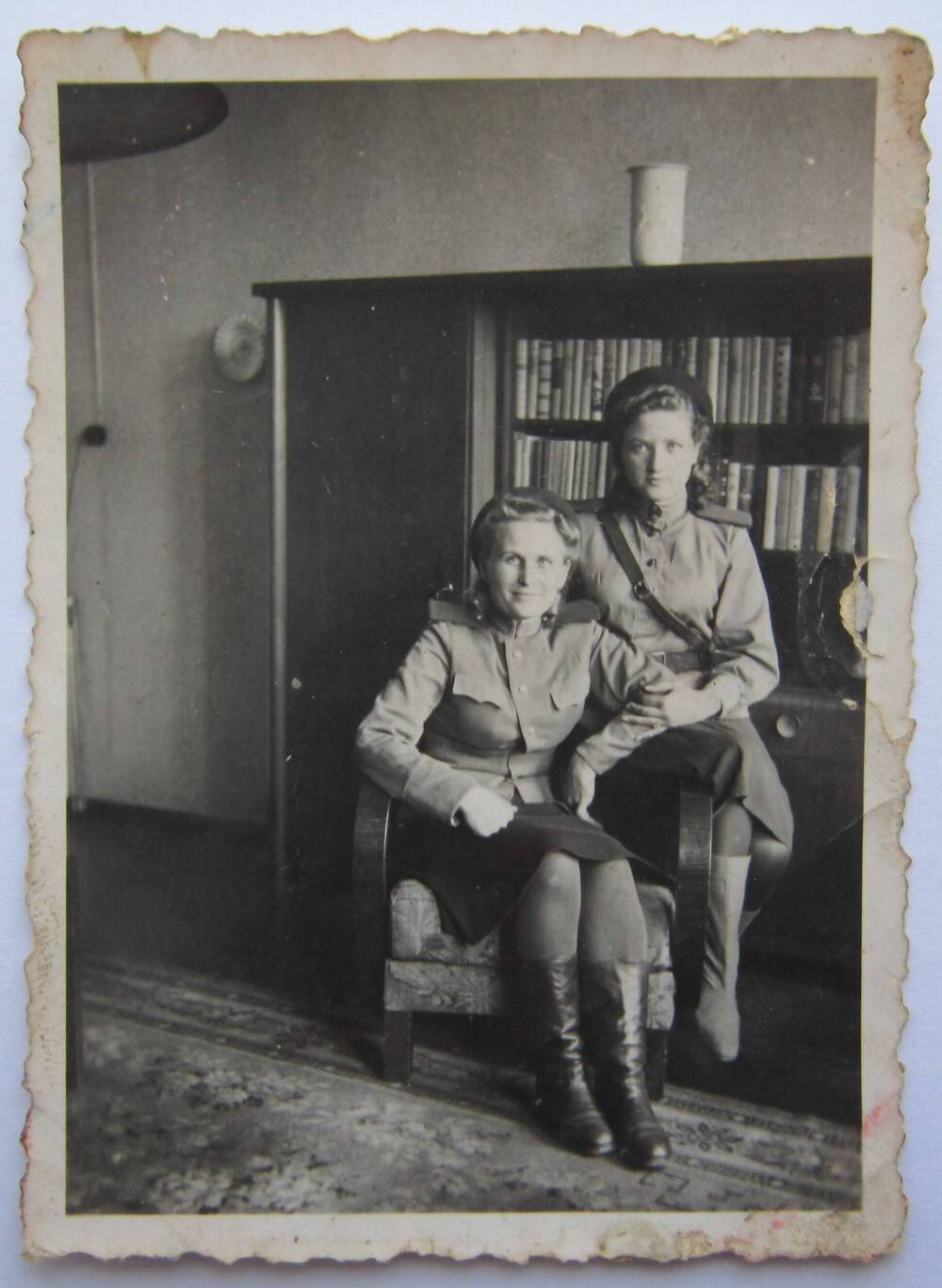 Фотоснимок. На фото две девушки в военной форме, сидящие на одном кресле. На заднем плане виден большой шкаф с книгами. 40-е годы.
Коллекция фотографий 40-50-х годов, собранная 
Березнёвой М. А.