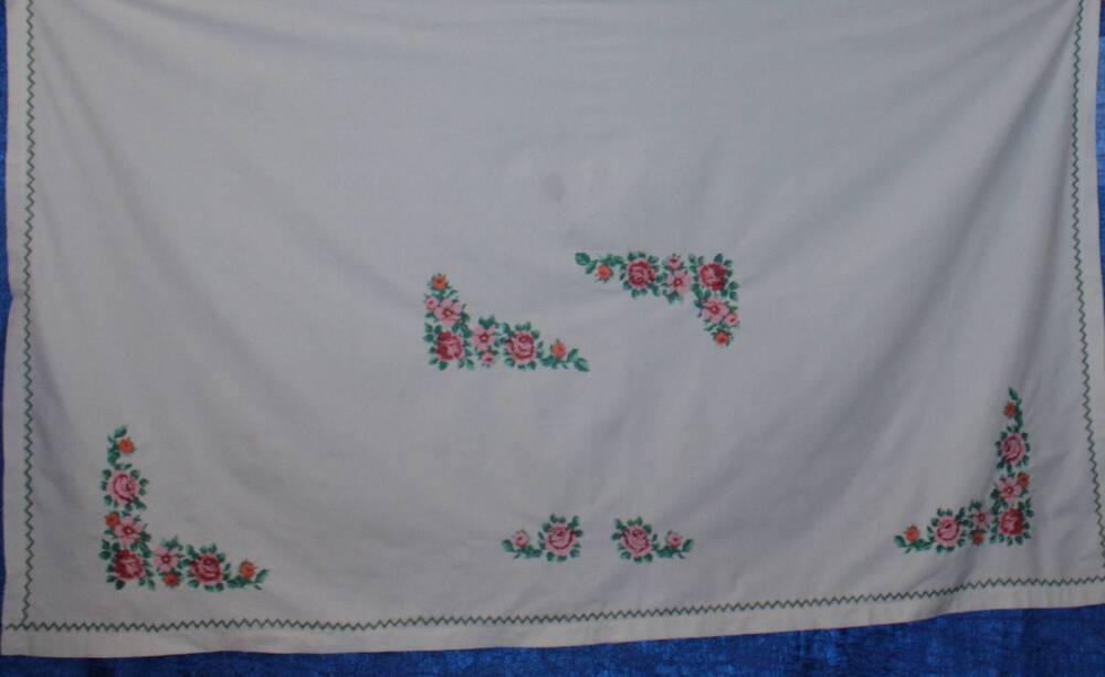 Скатерть украшенная вышивкой из роз и маков, вышивка по углам и центру скатерти. С 3 - х сторон кайма зелёного цвета.