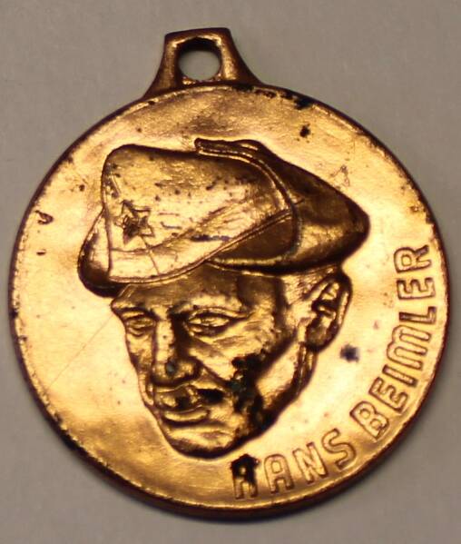 Значок имеет форму круга золотого цвета. На значке изображён в профиль портрет Ганса Бемлера. Значок при помощи ушка прикрепляется к колодочке в форме флага и винтовки.