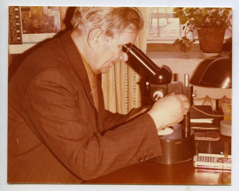 Фотография цветная. Кринов Е.Л. за микроскопом, изучающий микрометеориты из частной коллекции Вальтера Зейтцеля в г. Ханау ФРГ.