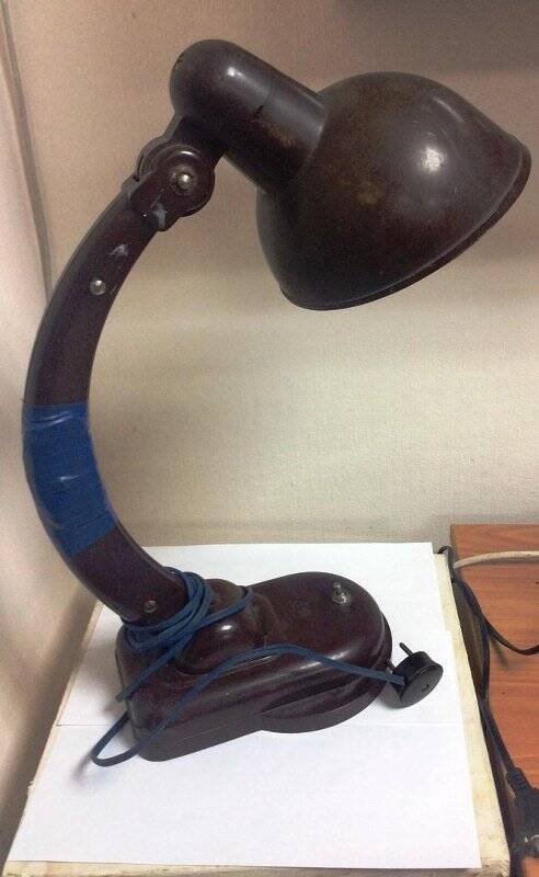 Лампа настольная (в народе называли «Лампа-НКВД») карболитовая коричневого цвета, на изогнутой ножке с шарниром-креплением на фигурной подставке.