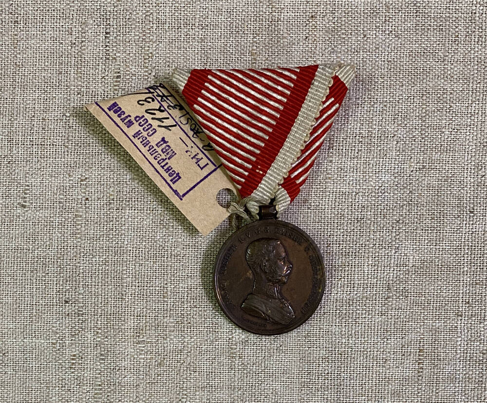 Медаль круглой формы Австро-Венгерской империи, на аверсе изображен силуэт человека, текст, на муаровой ленте