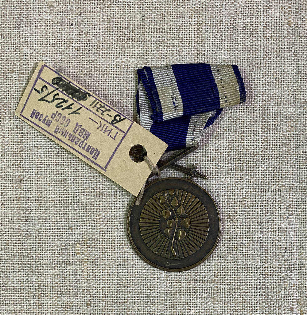 Медаль круглой формы с изображением трех воинов в касках, текст - на аверсе; на реверсе - ветка и перекрещивающиеся шпаги, на муаровой ленте