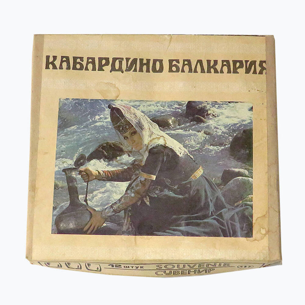 Коробка упаковочная набора стеклянных стопок «Кабардино-Балкария (сувенир)». Картонная, на бумажной наклейке фотоизображение горянки с кмганом у реки. СССР, 1973 г.
