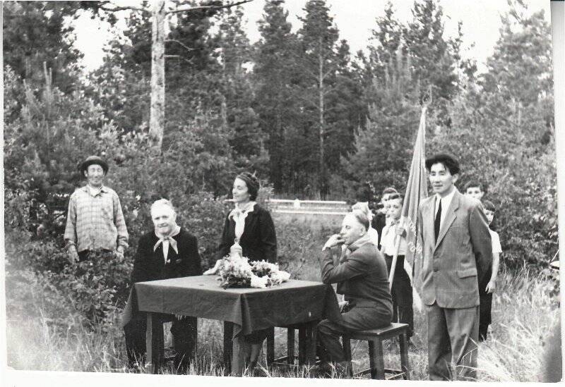 Фотография ч/б. Ветераны у пионер лагеря «Якутск», 1961 год. Сидят за столом слева-В. Никонов, в середине выступает Л.Транская, справа А.Транский.