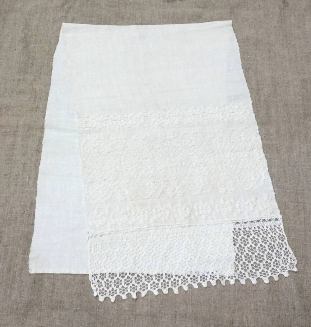 Половина домотканого белого полотенца, на одном конце которого выткан узор из белых ниток и кружева