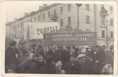 Фотография черно-белая. Участники демонстрации (цех автоматики и теплового контроля) движутся по одной из улиц г. Новокузнецка.