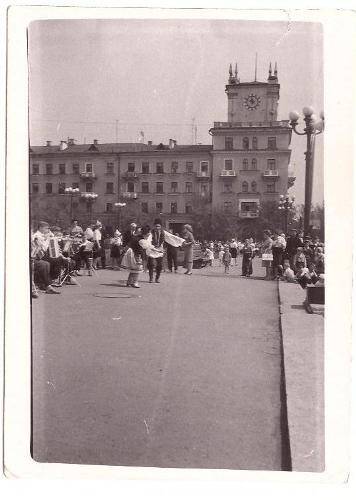 Фотография черно-белая. Участники танцевального коллектива  на фоне дома с башней с часами.