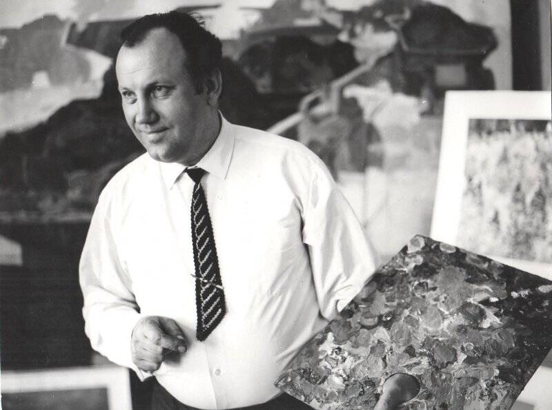 Фотография черно-белая. Лой Николай Павлович в мастерской с палитрой на фоне живописной картины