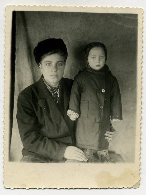 Фото. Групповой снимок. Мужчина сидит в пальто и шапке, ребенок стоит в пальто и платке, валенках.
