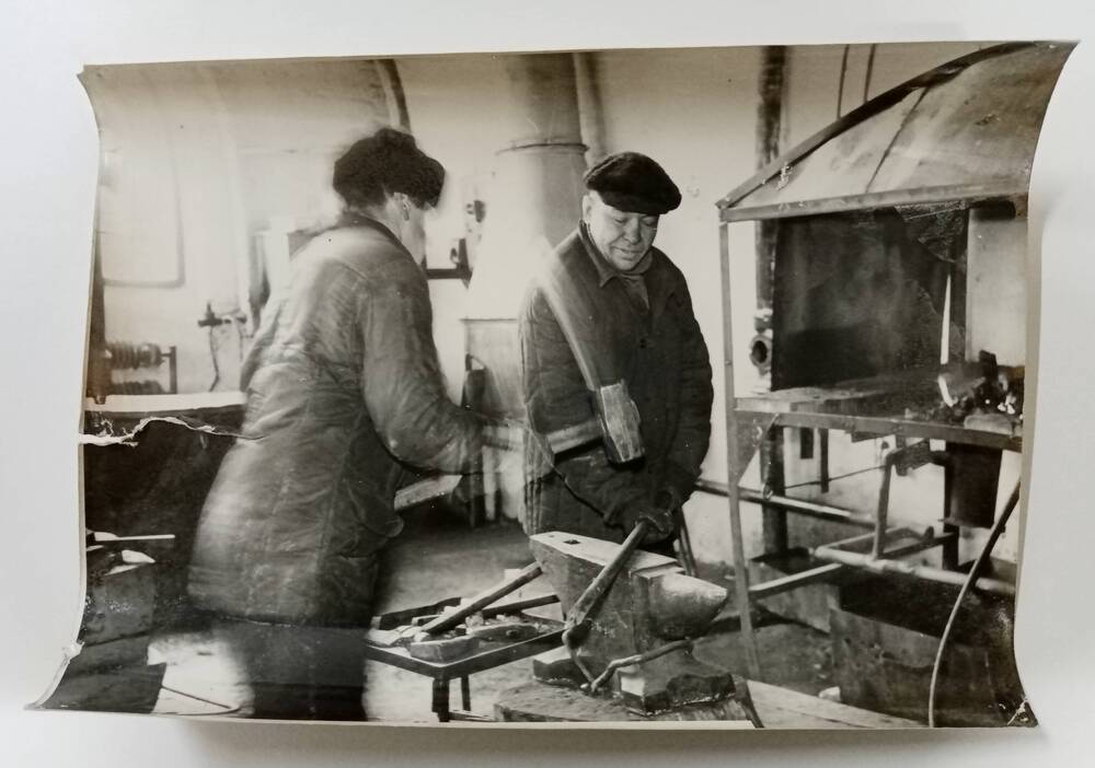 Фотография Олехова Архипа Архиповича, (справа) - кузнеца совхоза Орджоникидзевский, во время работы в кузнечном цехе РТМ.