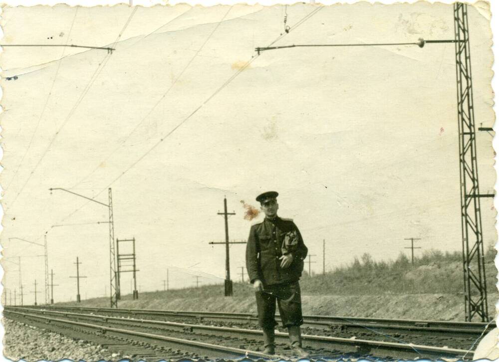 Фотография чёрно-белая: Лысюк Алексей Яковлевич стоит на ж/д путях в форме.